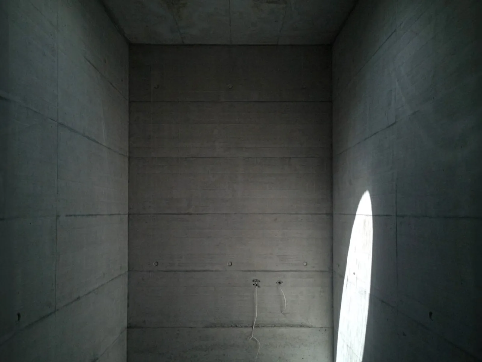 Minimalistischer Betonraum mit Oberlicht und Lichteinfall, der die schlichte Architektur betont.