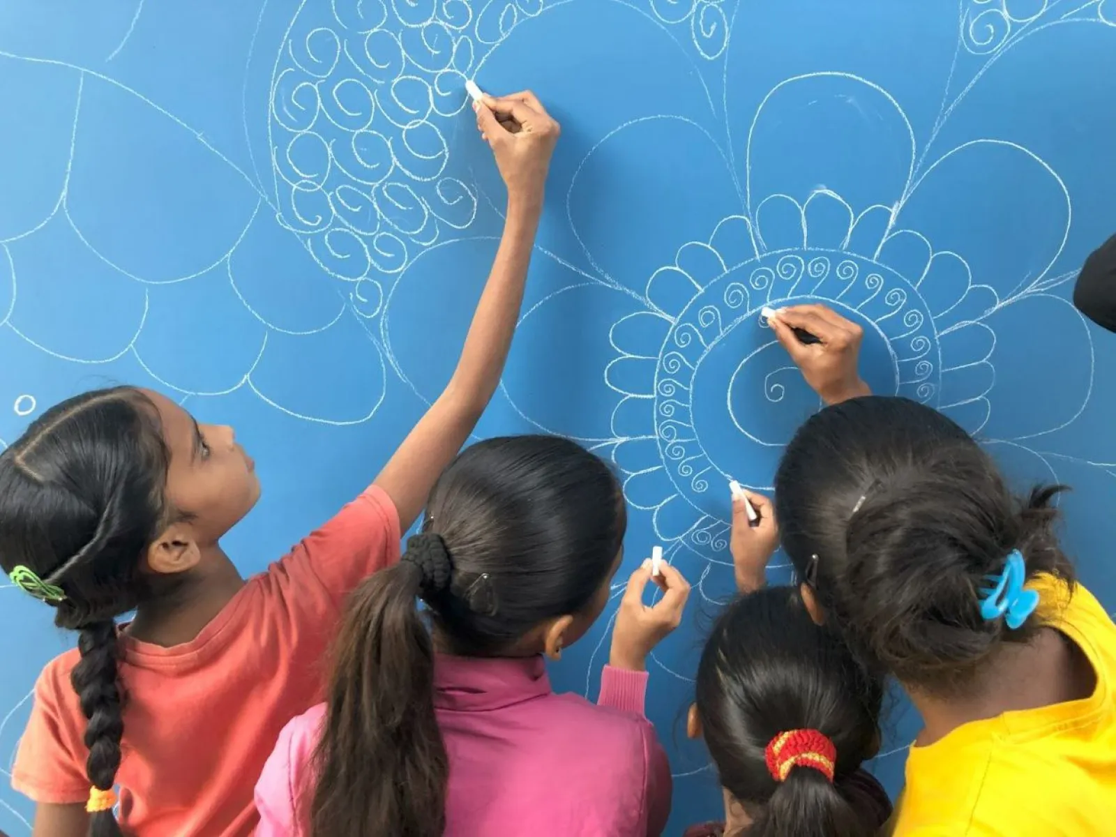 Kinder zeichnen mit Kreide auf eine blaue Tafel kunstvolle Muster.