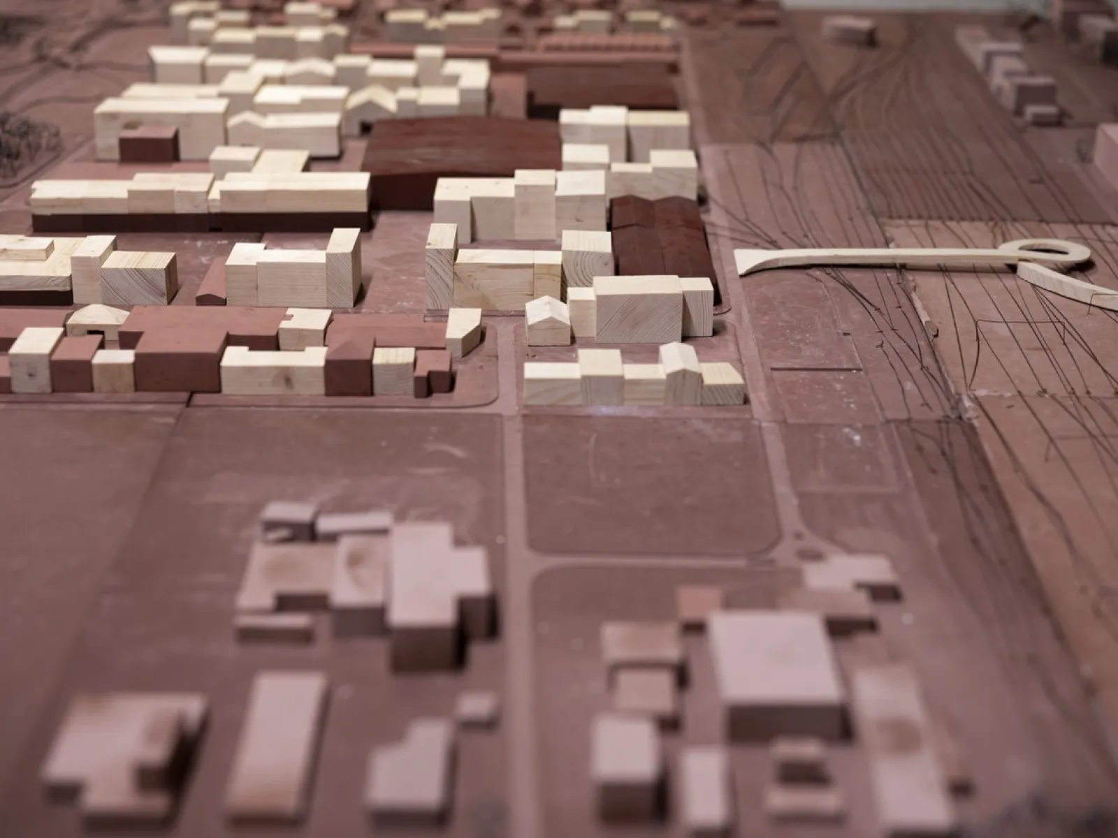 Ein Architekturmodell zeigt eine städtische Umgebung mit Gebäuden in verschiedenen Größen und Formen. Die Struktur besteht aus hellen und dunklen Holzblöcken, die Straßen und Freiflächen umgeben. Das Modell veranschaulicht städtebauliche Planung und Design.