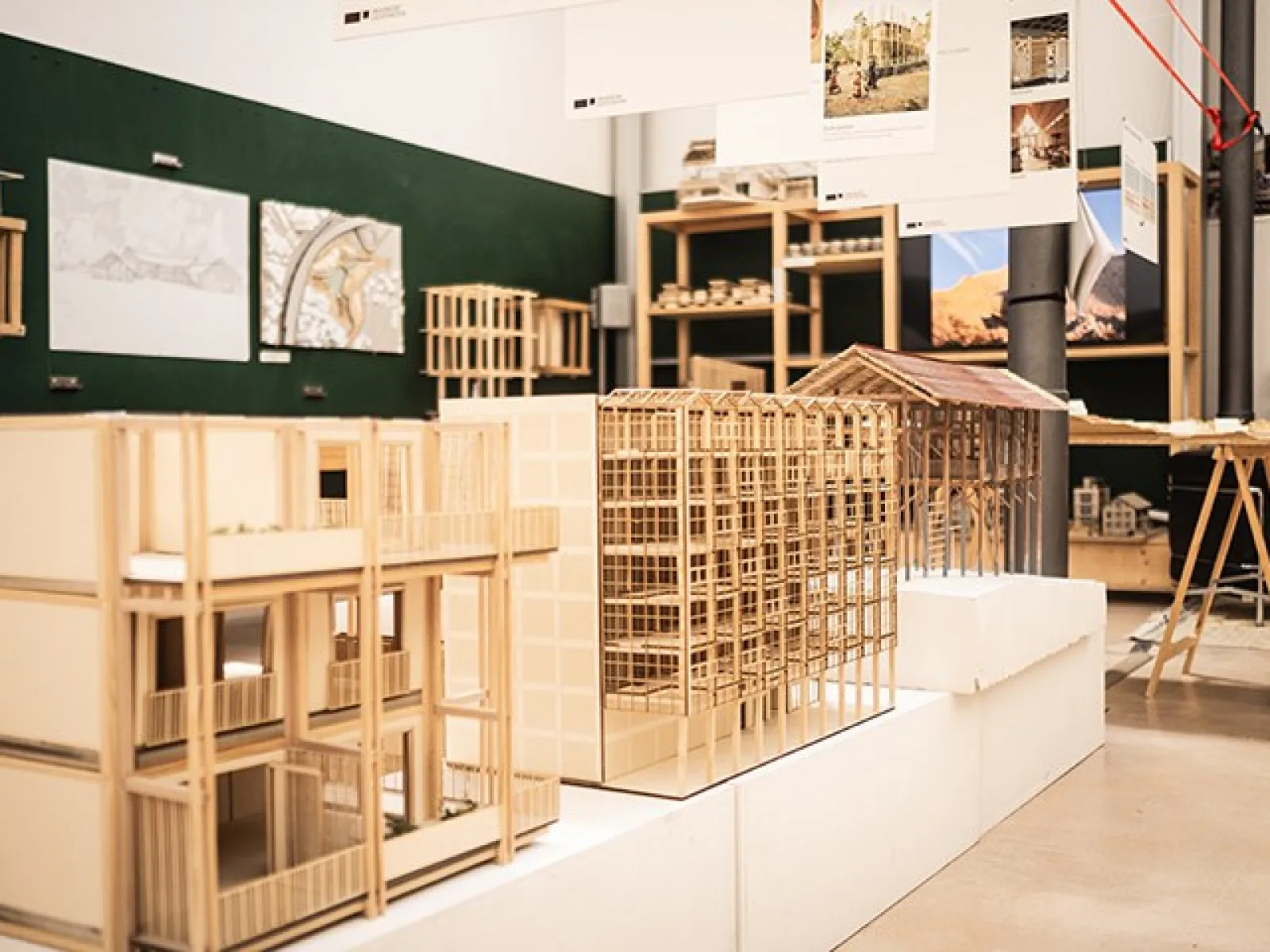 Architekturmodelle aus Holz in einem Ausstellungsraum der Universität Liechtenstein. Die Modelle zeigen detaillierte Gebäudestrukturen und sind Teil der Präsentation der Liechtenstein School of Architecture. Im Hintergrund sind Pläne und weitere Modelle sichtbar.