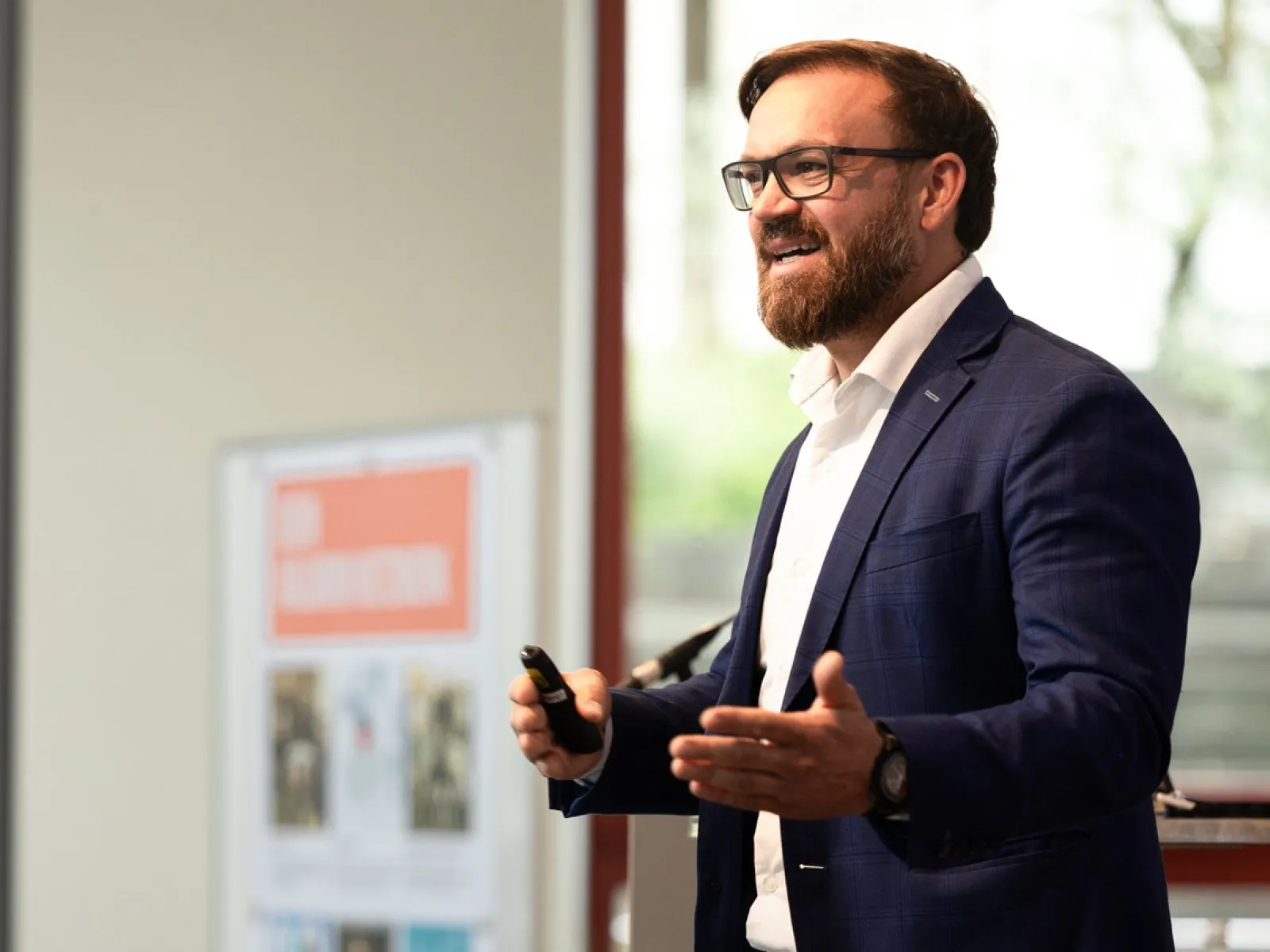 Auf dem Bild ist der Studiengangsmanager des Masters in Entrepreneurship & Management Tobias Fitz zu sehen wie er gerade eine Rede hält. Er trägt einen blauen Anzug mit einem weissen Hemd.