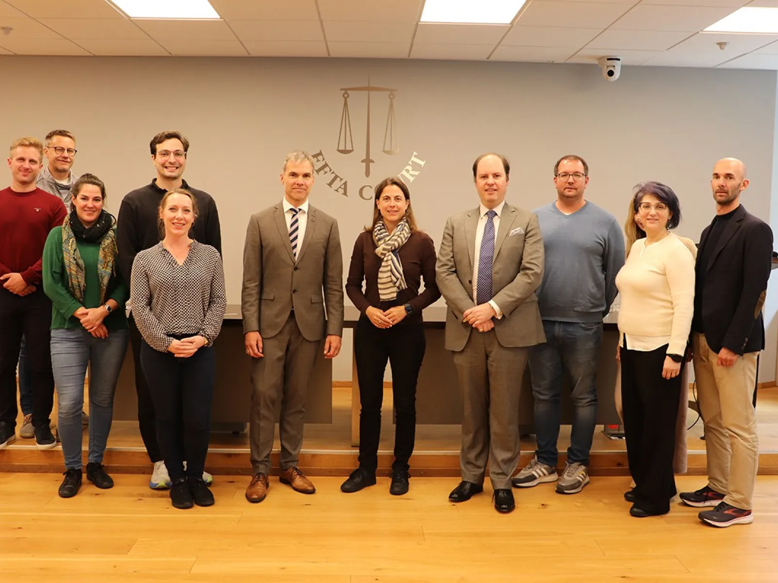 Eine Gruppe von Studierenden und Dozenten des Executive Master of Laws (LL.M.) im Wirtschaftsstrafrecht steht in einem Konferenzraum vor einer Wand mit dem Logo des EFTA Court. Sie sind formell gekleidet und lächeln in die Kamera.