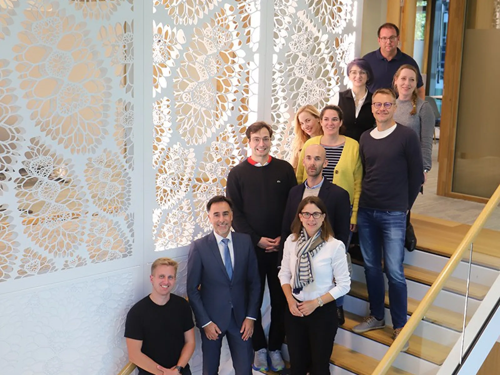 Gruppe von Studierenden und Dozenten des Executive Master of Laws (LL.M.) im Wirtschaftsstrafrecht auf einer Treppe, umgeben von dekorativen Wandpaneelen, während einer Studienreise in Den Haag.