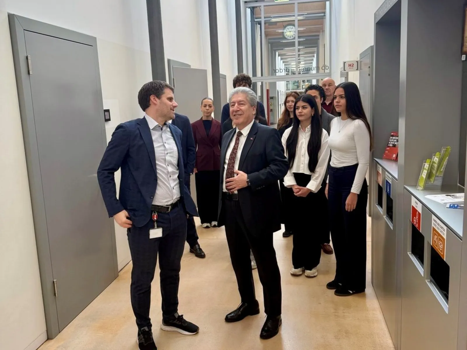 Gruppe von Menschen in einem modernen Universitätsflur, darunter ein Mann im Anzug, der spricht. Im Hintergrund sind weitere Personen, die aufmerksam zuhören. Die Szene zeigt einen offiziellen Besuch und Austausch an der Universität Liechtenstein.