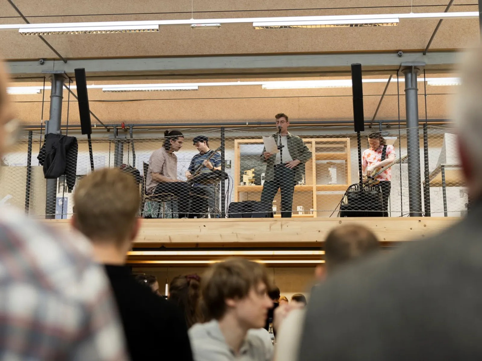 Eine Band spielt auf einer erhöhten Bühne in einem Innenraum. Im Vordergrund sind unscharf Menschen zu sehen, die dem Auftritt zuschauen. Die Szene wirkt lebhaft und ist Teil einer Veranstaltung an der Universität Liechtenstein.