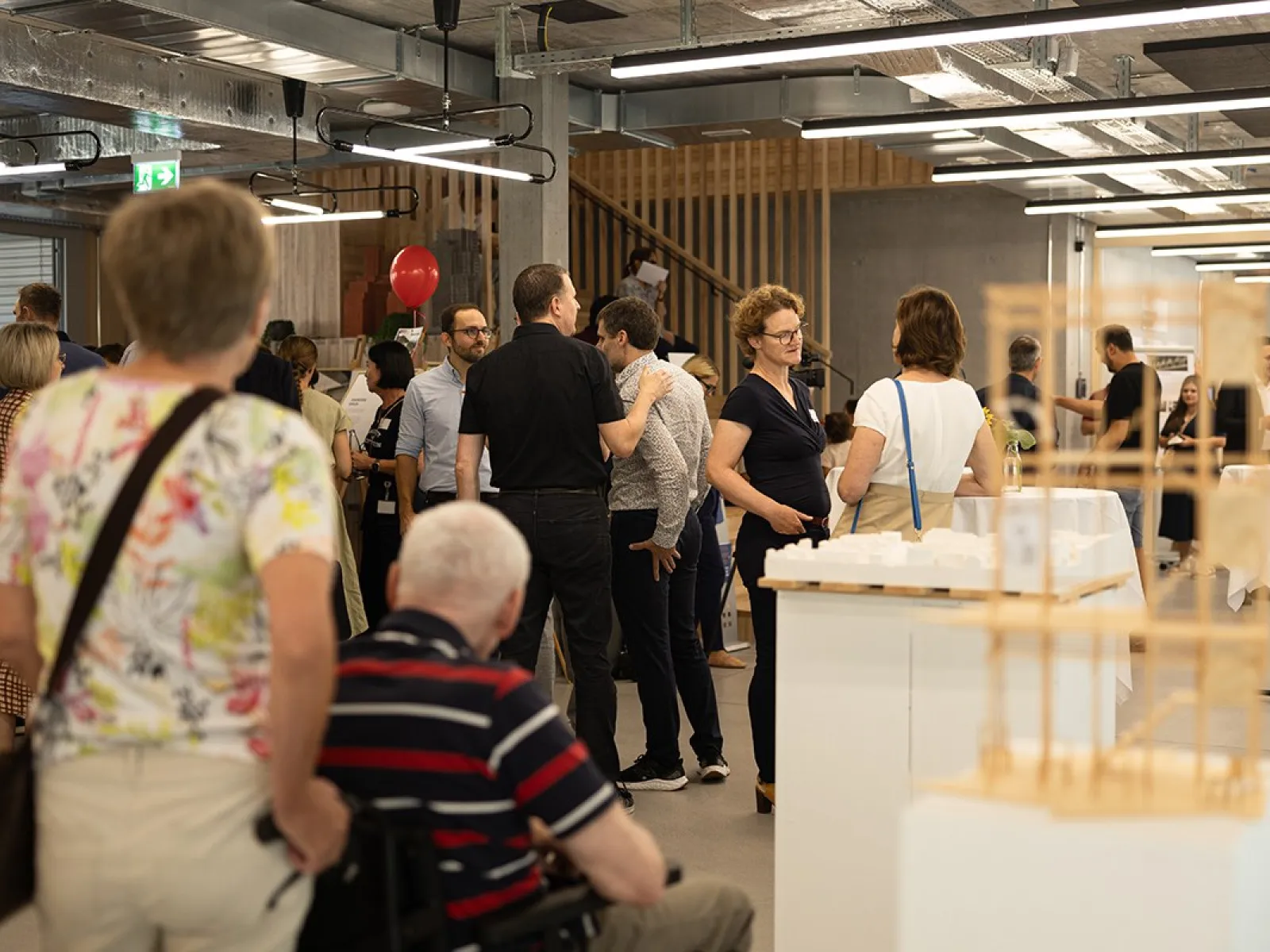 Besucherinnen und Besucher erkunden den neuen Standort der Universität Liechtenstein während des Tags der offenen Tür. Menschen stehen in einem modernen Innenraum, unterhalten sich und betrachten Ausstellungsstücke.