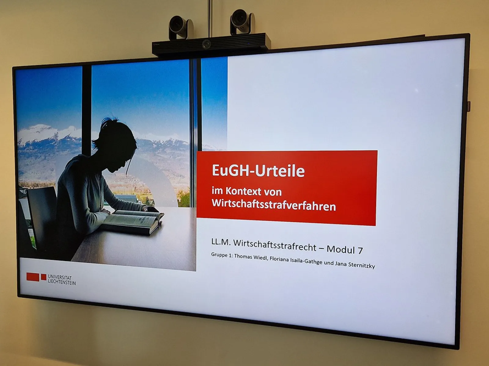 Ein Bildschirm zeigt eine Präsentation mit dem Titel "EuGH-Urteile im Kontext von Wirtschaftsstrafverfahren". Links ist eine Person am Laptop vor einem Fenster mit Bergblick zu sehen. Unten steht "LL.M. Wirtschaftsstrafrecht – Modul 7" und die Namen der Gruppenmitglieder.