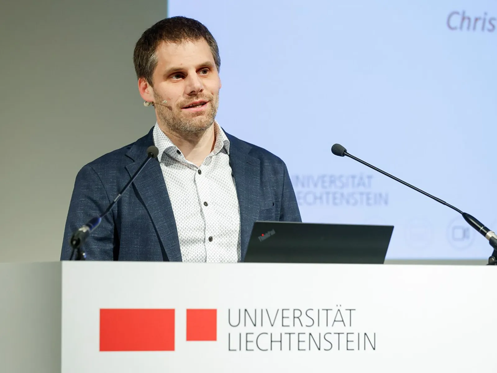 Der Rektor der Universität Liechtenstein Christian Frommelt steht an einem Redepult mit dem Logo der Universität aufgedruckt.