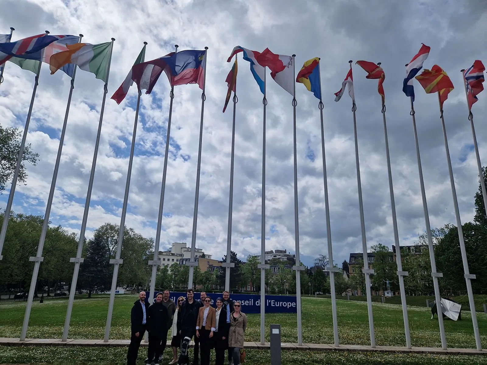 Gruppe von Studierenden vor dem Europarat in Straßburg, umgeben von internationalen Flaggen, während einer Studienreise des Executive Master of Laws im Wirtschaftsstrafrecht.