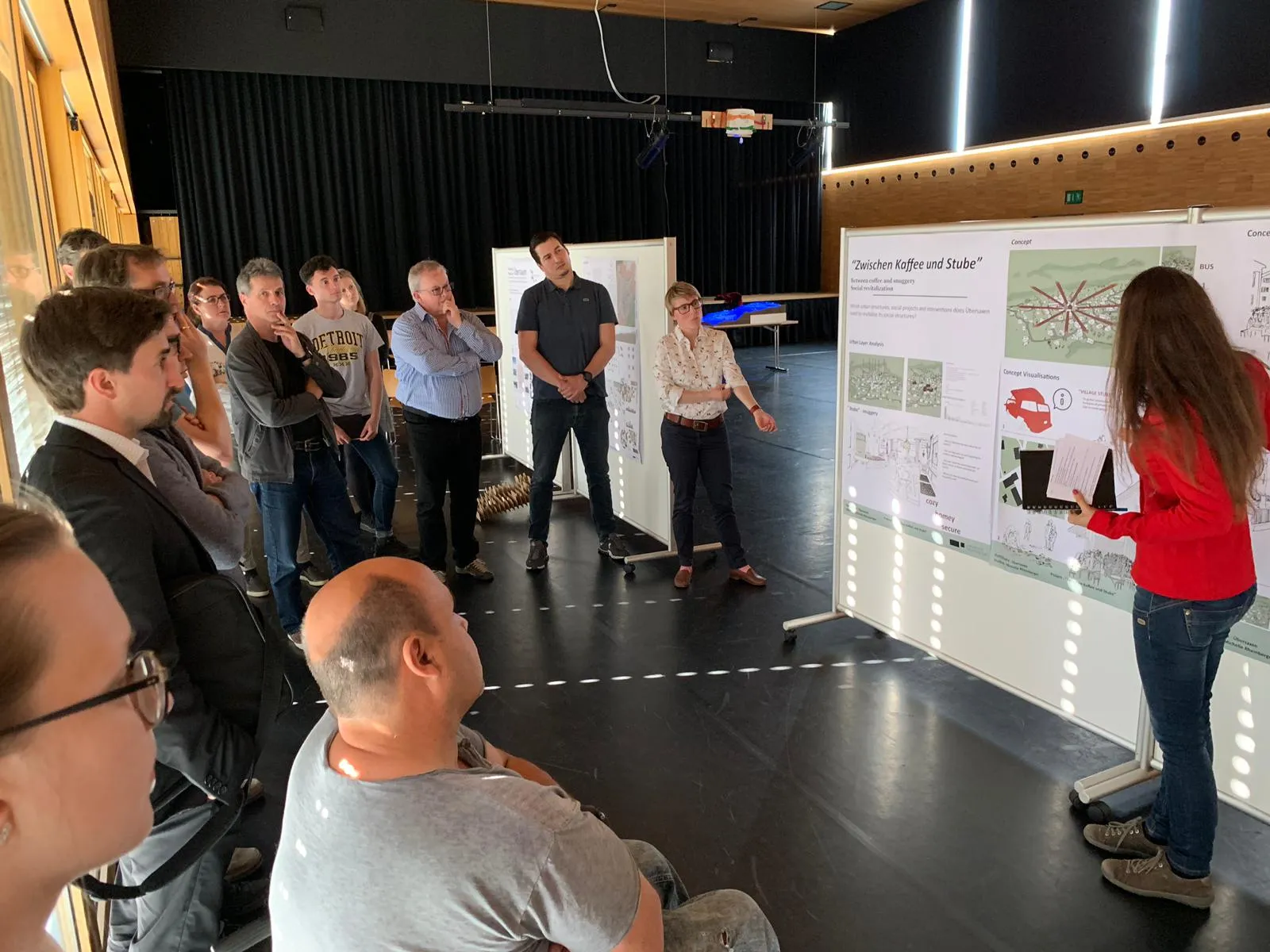 Mehrere Menschen bei einer Präsentation einer Studentin mit Architekturprojekten an einer Pinnwand