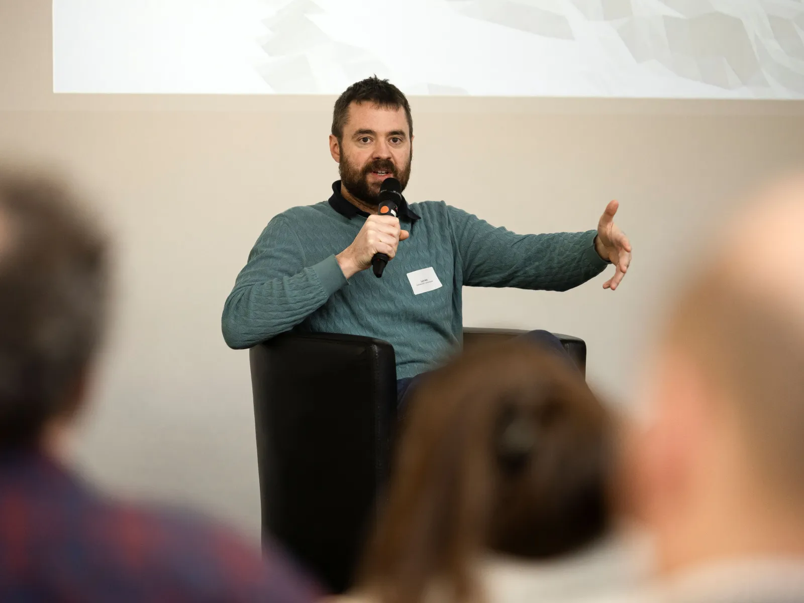 Mann mit blauem Pullover auf Podium mit Mikrofon