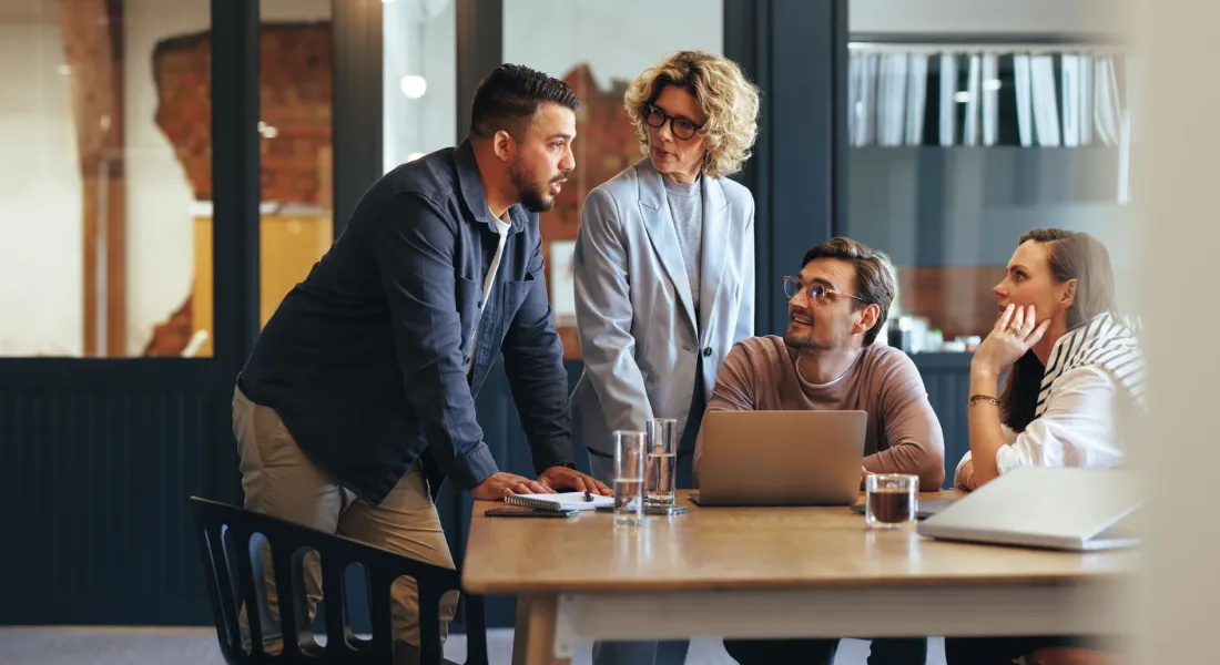  Eine Gruppe von Personen sitzt um einen Tisch mit einem Laptop und diskutiert angeregt miteinander.