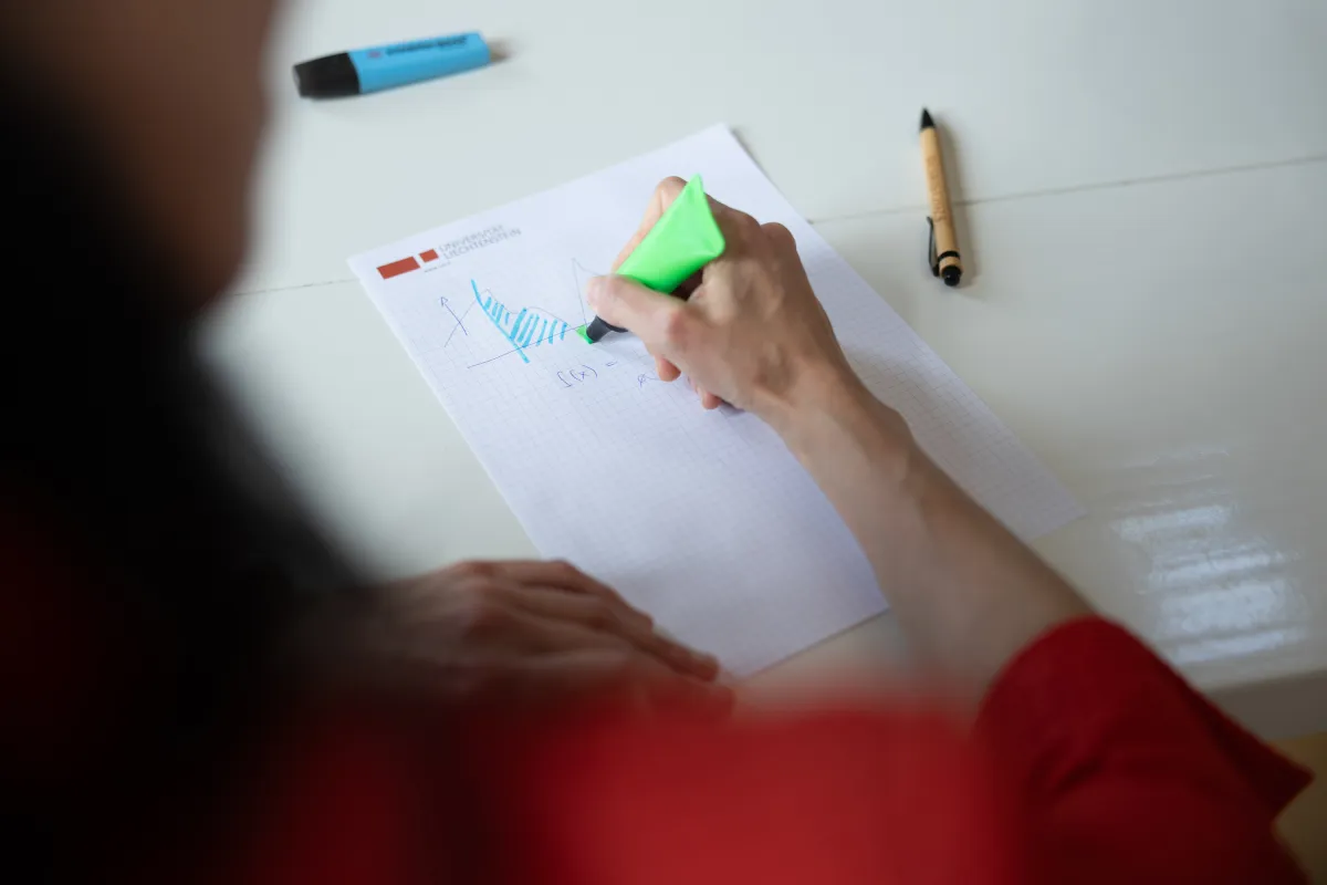 Detailaufnahme einer Hand beim Markieren eines Funktionsgraphen auf Uni-Papier mit grünem Textmarker.