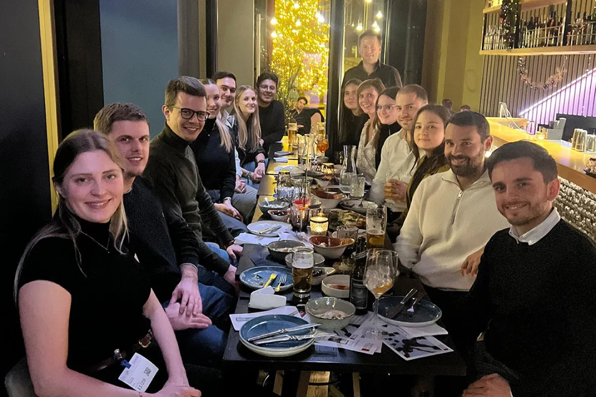 Eine Gruppe von Alumni der Universität Liechtenstein sitzt in einem Restaurant an einem langen Tisch, lächelnd und in geselliger Runde. Auf dem Tisch stehen Getränke und Teller mit Speisen. Die Atmosphäre ist warm und einladend.