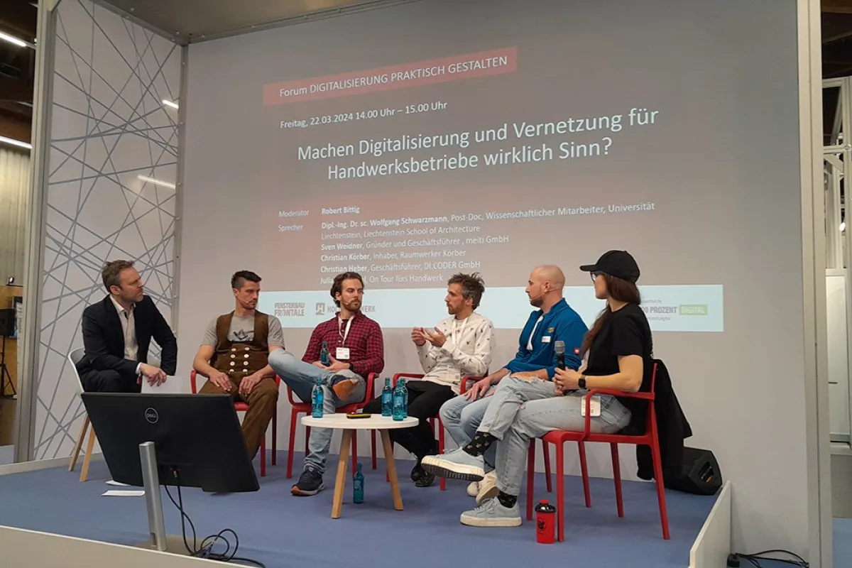 Podiumsdiskussion auf der Messe «Holz Handwerk 2024» in Nürnberg. Fünf Personen sitzen auf einer Bühne vor einer Leinwand mit dem Titel "Machen Digitalisierung und Vernetzung für Handwerksbetriebe wirklich Sinn?". Die Diskussion thematisiert die Rolle der Digitalisierung im Handwerk.
