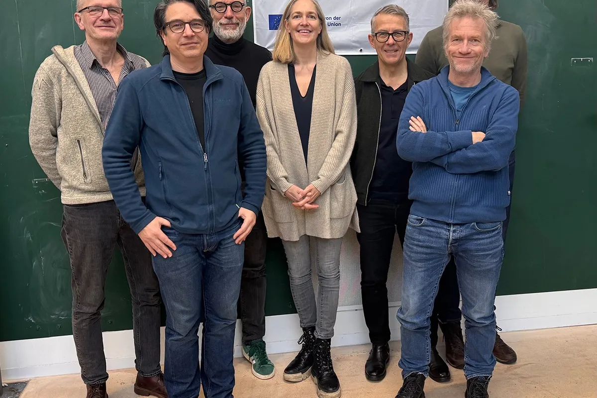 Eine Gruppe von acht Personen steht vor einem grünen Hintergrund. Sie lächeln in die Kamera. Im Hintergrund hängt ein Banner mit der Aufschrift "Erasmus+ Neue Perspektiven, Neue Horizonte".