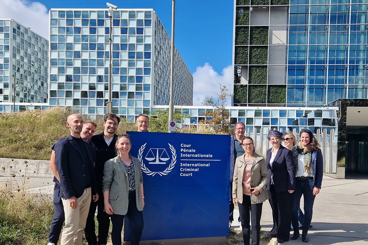 Gruppe von Studierenden des Executive Master of Laws (LL.M.) im Wirtschaftsstrafrecht vor dem Internationalen Strafgerichtshof in Den Haag, lächelnd und posierend vor dem Gebäude mit dem Logo des Gerichtshofs.
