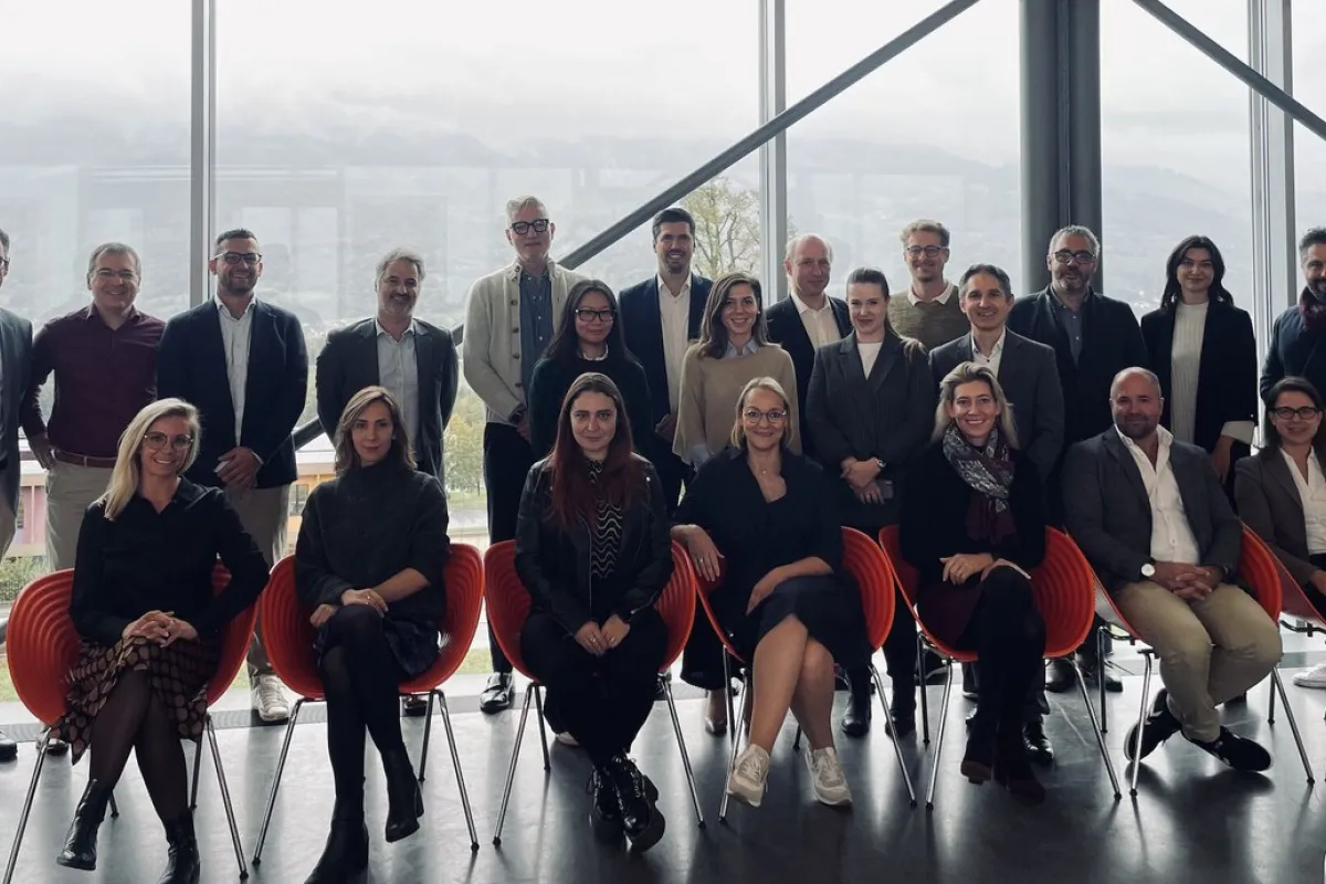 Gruppenfoto von Teilnehmenden der MiCAR Expert Roundtable Series an der Universität Liechtenstein. Die Personen stehen und sitzen in zwei Reihen vor einer großen Fensterfront mit Blick auf eine bergige Landschaft.
