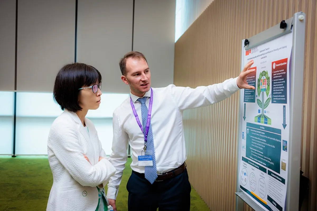 Ein Mann erklärt einer Frau ein wissenschaftliches Poster über nachhaltige Besteuerung in einem Konferenzraum.