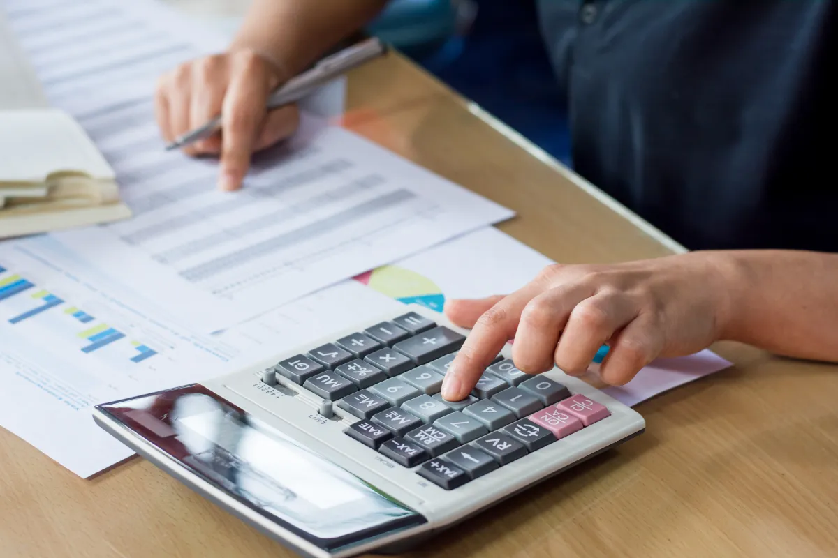 Person sitzt am Tisch mit Taschenrechner und Papier und rechnet