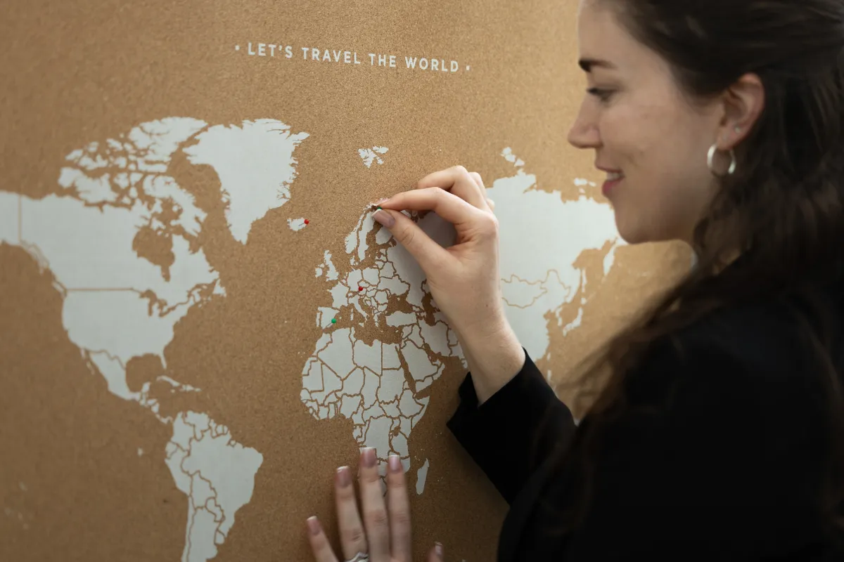 Frau steckt roten Pin in Weltkarte mit Aufschrift „Let’s Travel the World“.