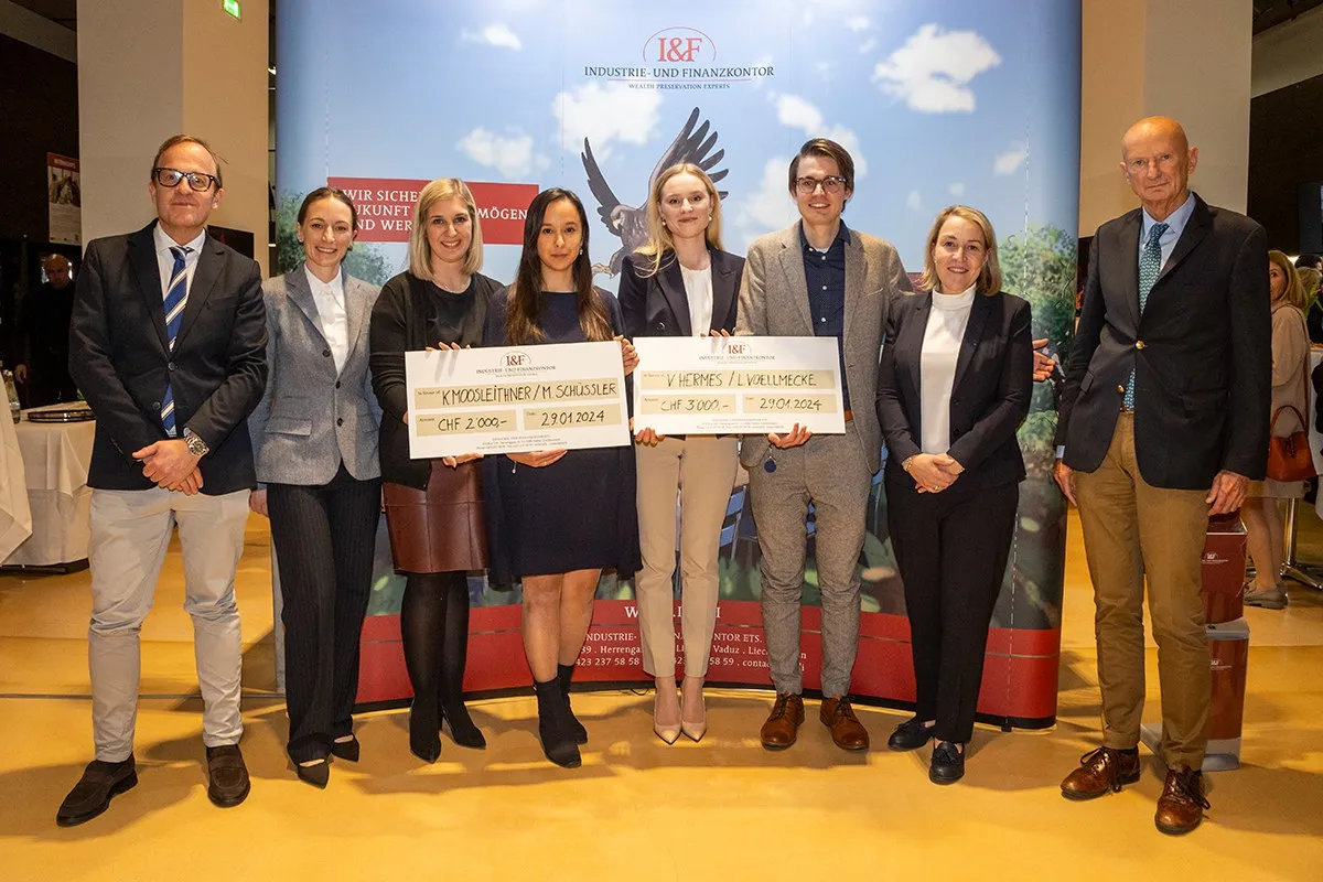Gruppe von acht Personen posiert mit zwei großen Schecks bei der Verleihung des I&F Family Wealth Preservation Awards an der Universität Liechtenstein. Die Studierenden wurden für ihre herausragenden Strukturierungsvorschläge ausgezeichnet. Im Hintergrund ist ein Banner des Industrie- und Finanzkontors zu sehen.