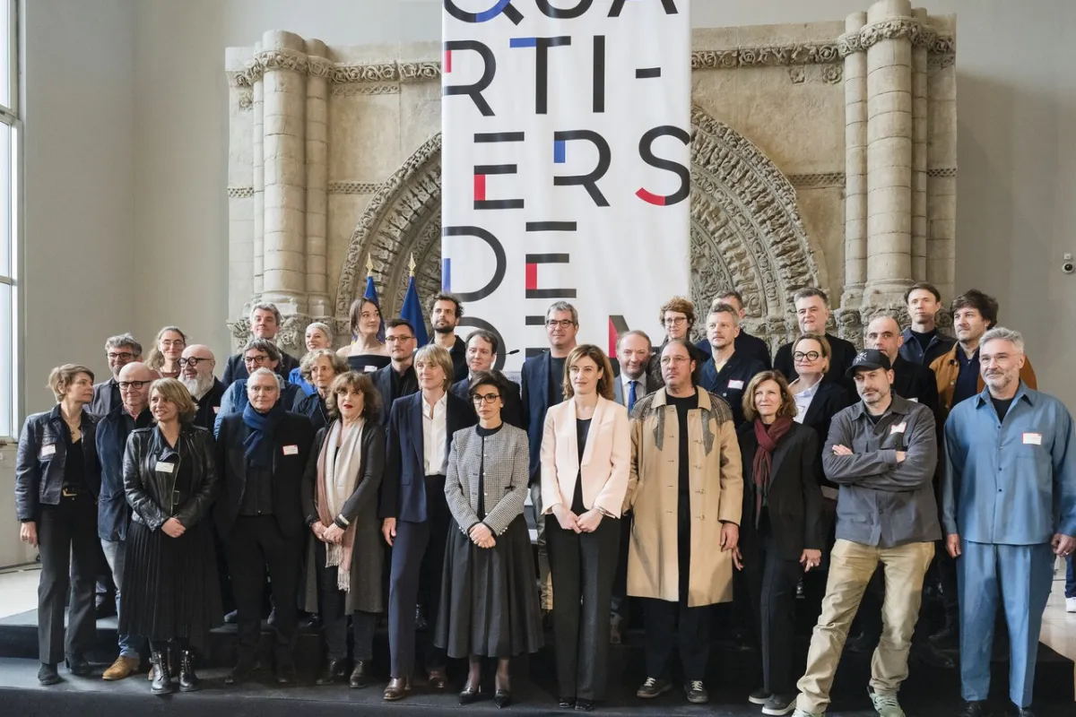 Gruppe von Architekten und Dozenten steht vor einem großen Banner mit der Aufschrift „Quartiers de demain“ in einem historischen Gebäude.