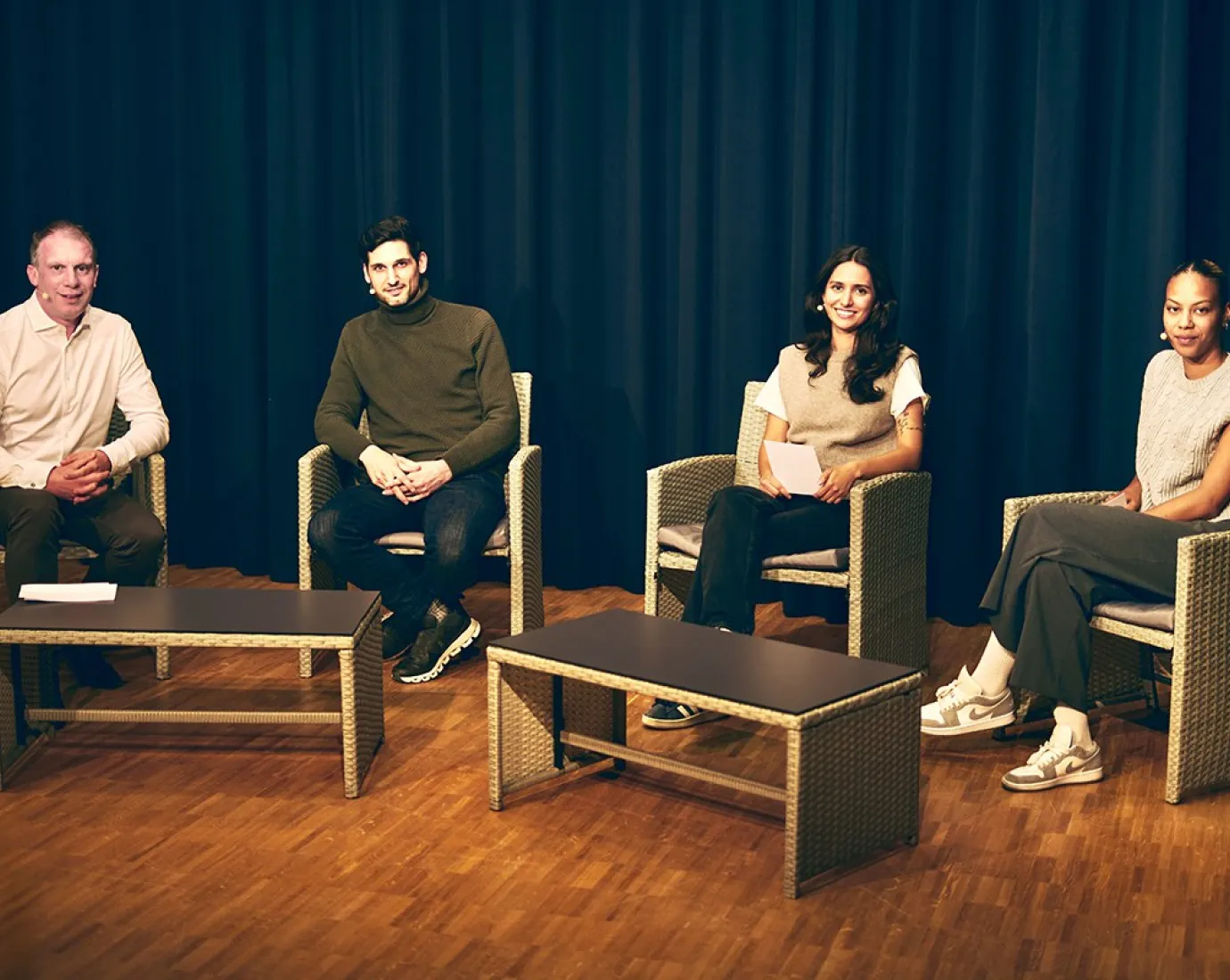 Vier Personen sitzen auf einer Bühne in Korbstühlen, vor einem dunklen Vorhang. Sie sind Teil einer Diskussionsrunde über Upcycling in der Architektur an der Universität Liechtenstein.