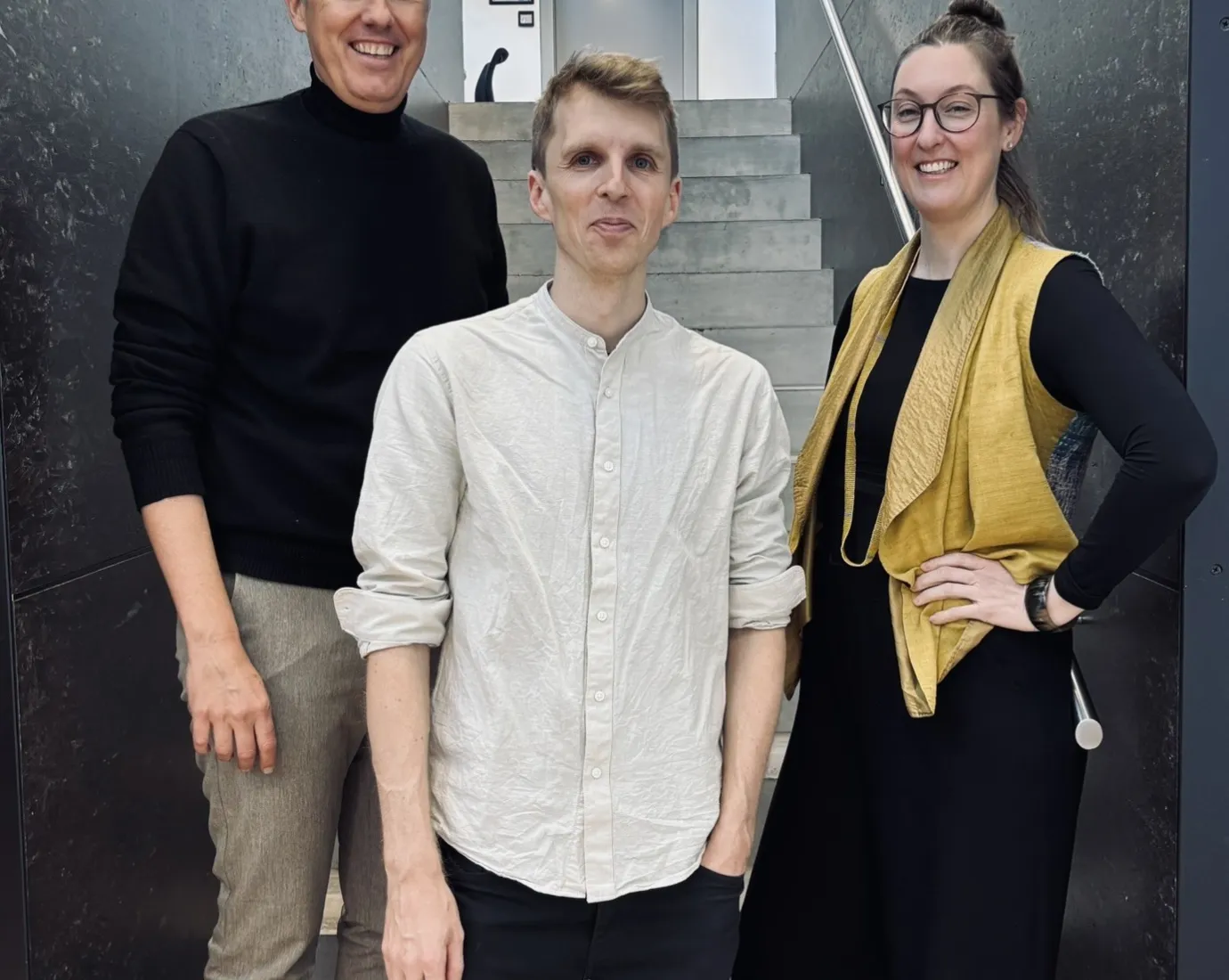 Drei Personen auf einer grau/schwarzen Treppe