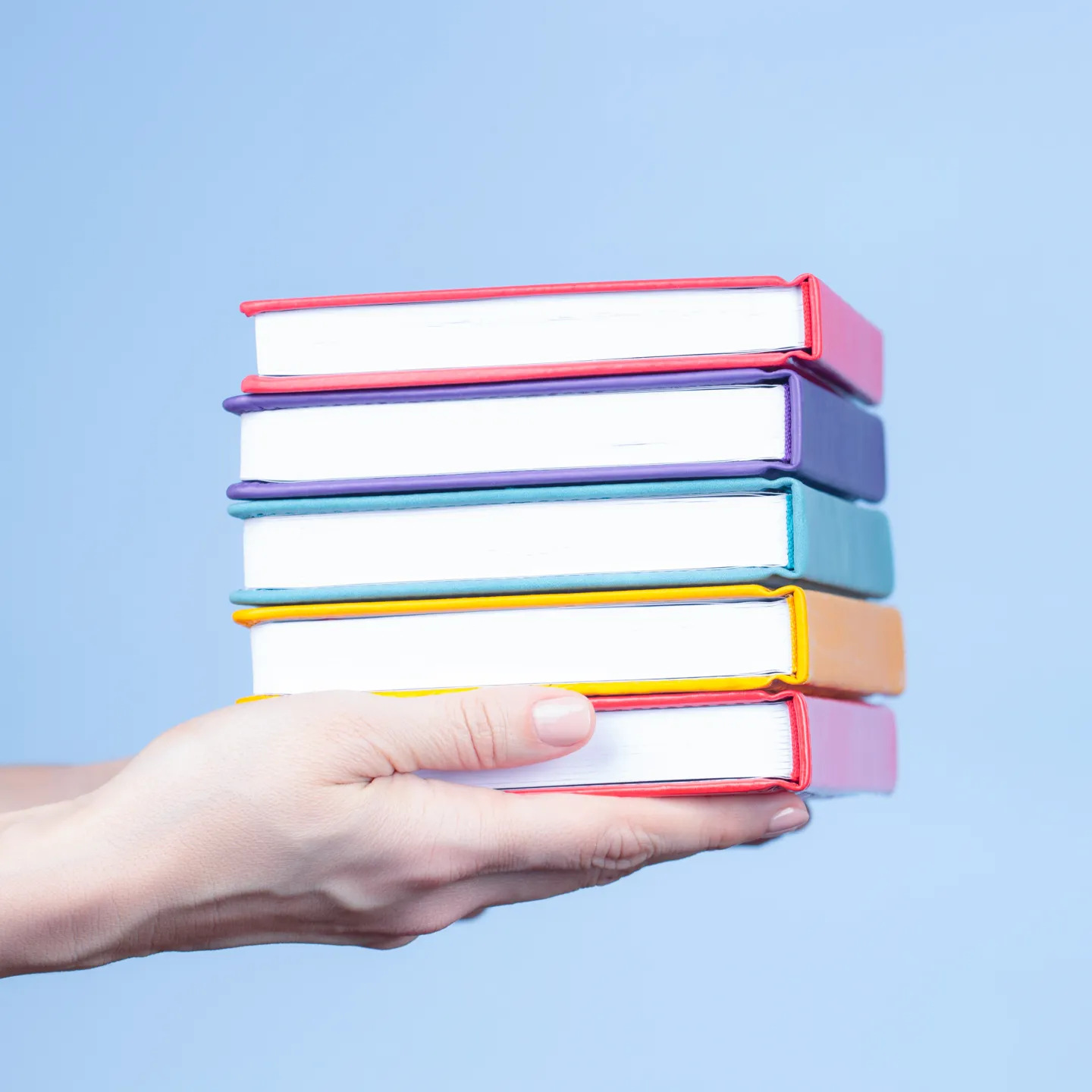 Hand haelt mehrere bunte Buecher vor hellblauem Hintergrund, Fokus auf Vielfalt und Bildung.