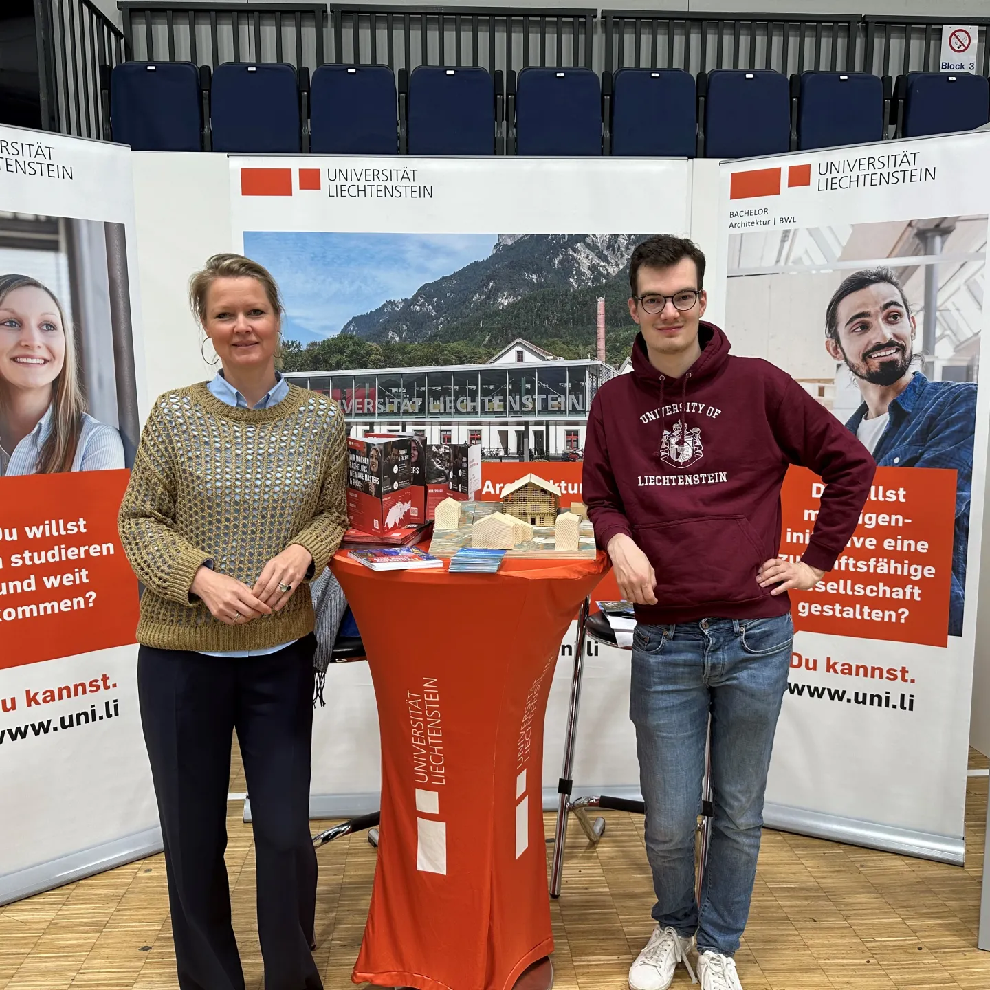 Messestand der Universität Liechtenstein in Düsseldorf mit Infomaterial und zwei Personen vor Informationsbannern.