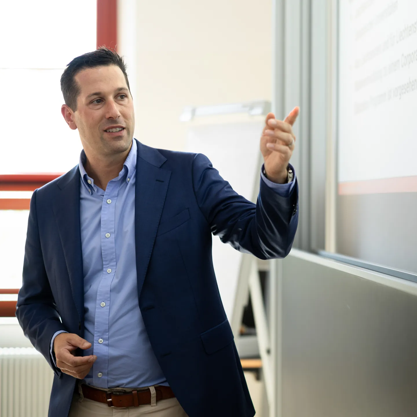 Nahaufnahme eines Dozenten, der auf eine Folie zeigt und einen Sachverhalt erklärt, im Unterricht an der Universität Liechtenstein.