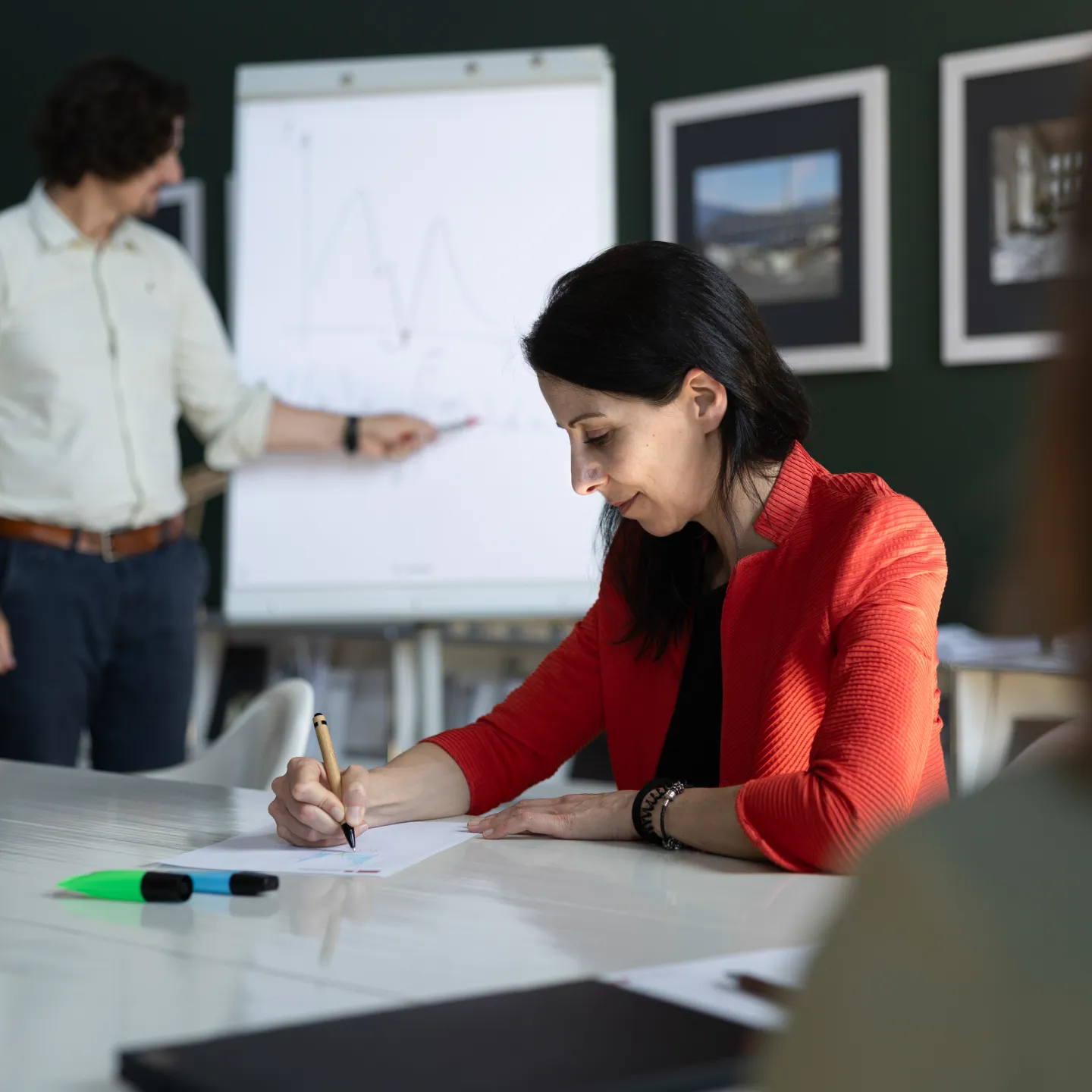 Dozent präsentiert mathematische Funktion an Flipchart, während eine Teilnehmerin aktiv mitschreibt.