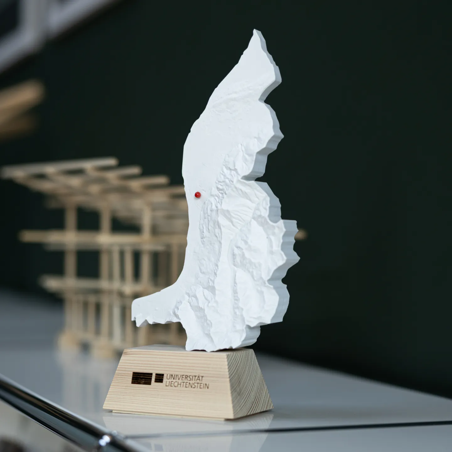 Modell des Fürstentums Liechtenstein mit Universitätslogo im Vordergrund, im Hintergrund Architekturmodelle als Teil einer studentischen Ausstellung.