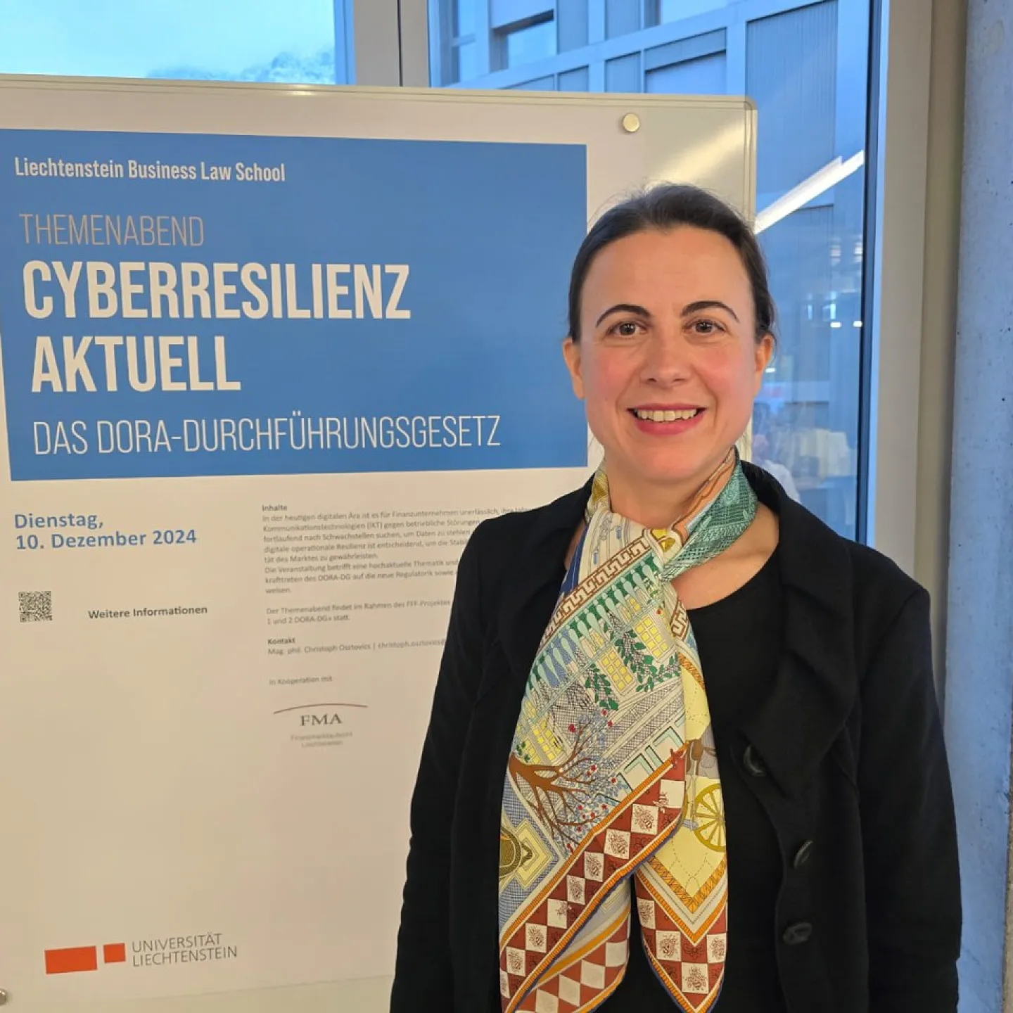 Frau steht lächelnd vor einem Plakat der Liechtenstein Business Law School. Das Plakat kündigt den Themenabend „Cyberresilienz aktuell: Das DORA-Durchführungsgesetz“ an, der am 10. Dezember 2024 stattfindet.