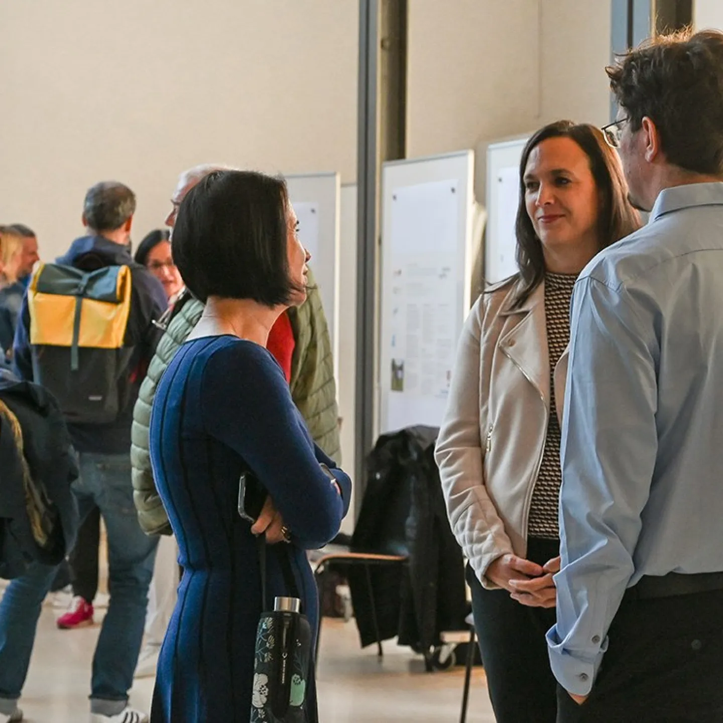 Menschen stehen in einem Auditorium der Universität Liechtenstein und unterhalten sich vor Ausstellungstafeln. Die Atmosphäre ist lebhaft, und die Veranstaltung scheint gut besucht zu sein.