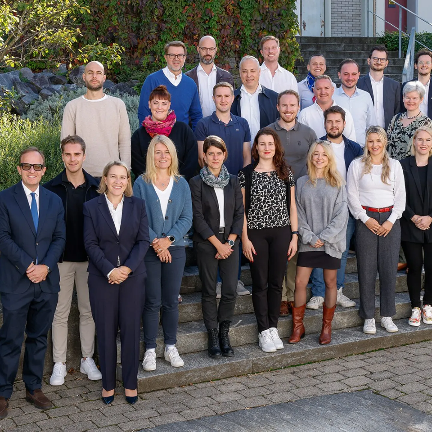 Gruppenfoto von Studierenden und Dozenten des Executive Master of Laws (LL.M.) im Gesellschafts-, Stiftungs- und Trustrecht an der Universität Liechtenstein. Die Gruppe steht auf einer Treppe im Freien, umgeben von grüner Vegetation.