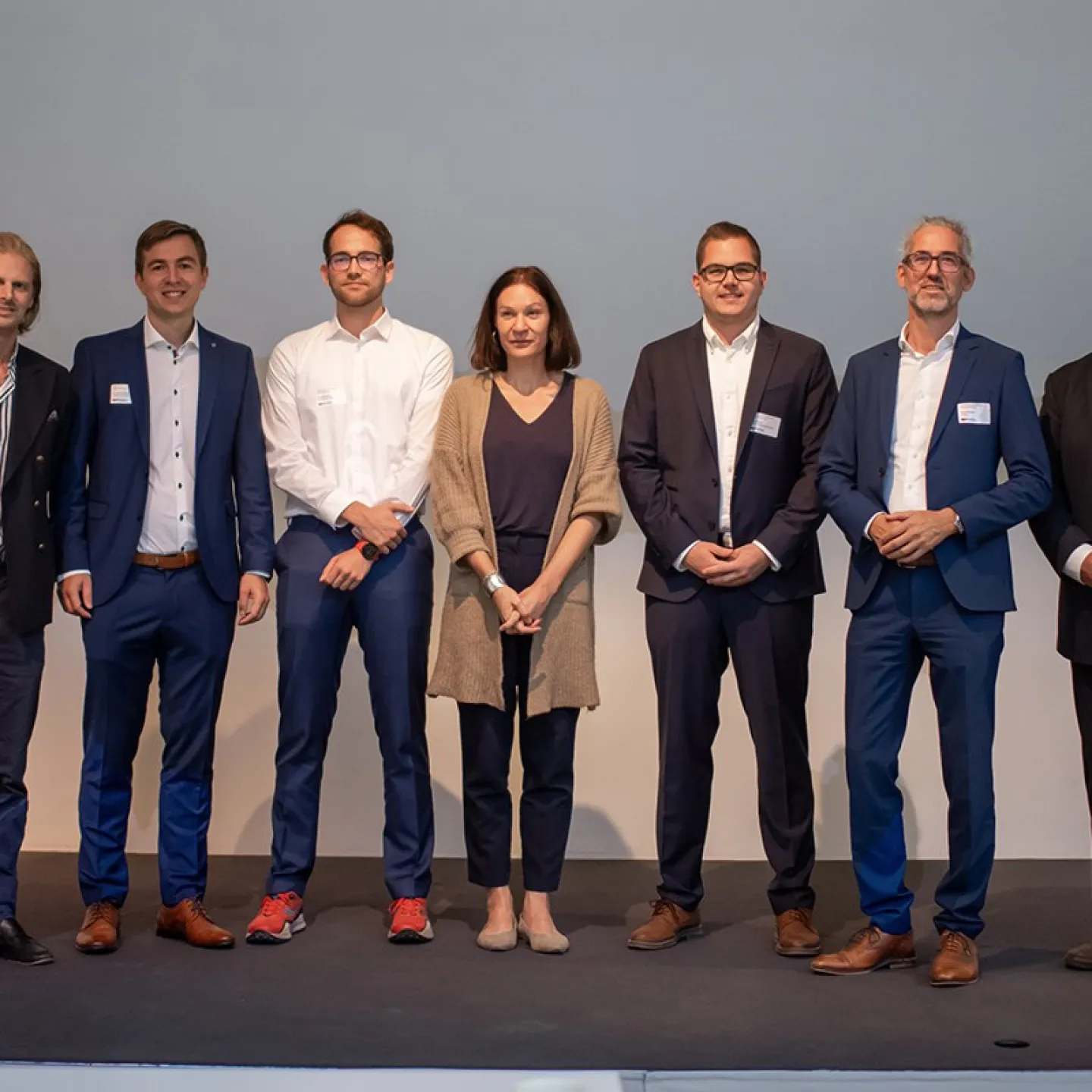 Eine Gruppe von sieben Personen steht auf einer Bühne beim 8. Liechtenstein Workshop of Sustainable Finance an der Universität Liechtenstein. Sie tragen formelle Kleidung und lächeln in die Kamera.