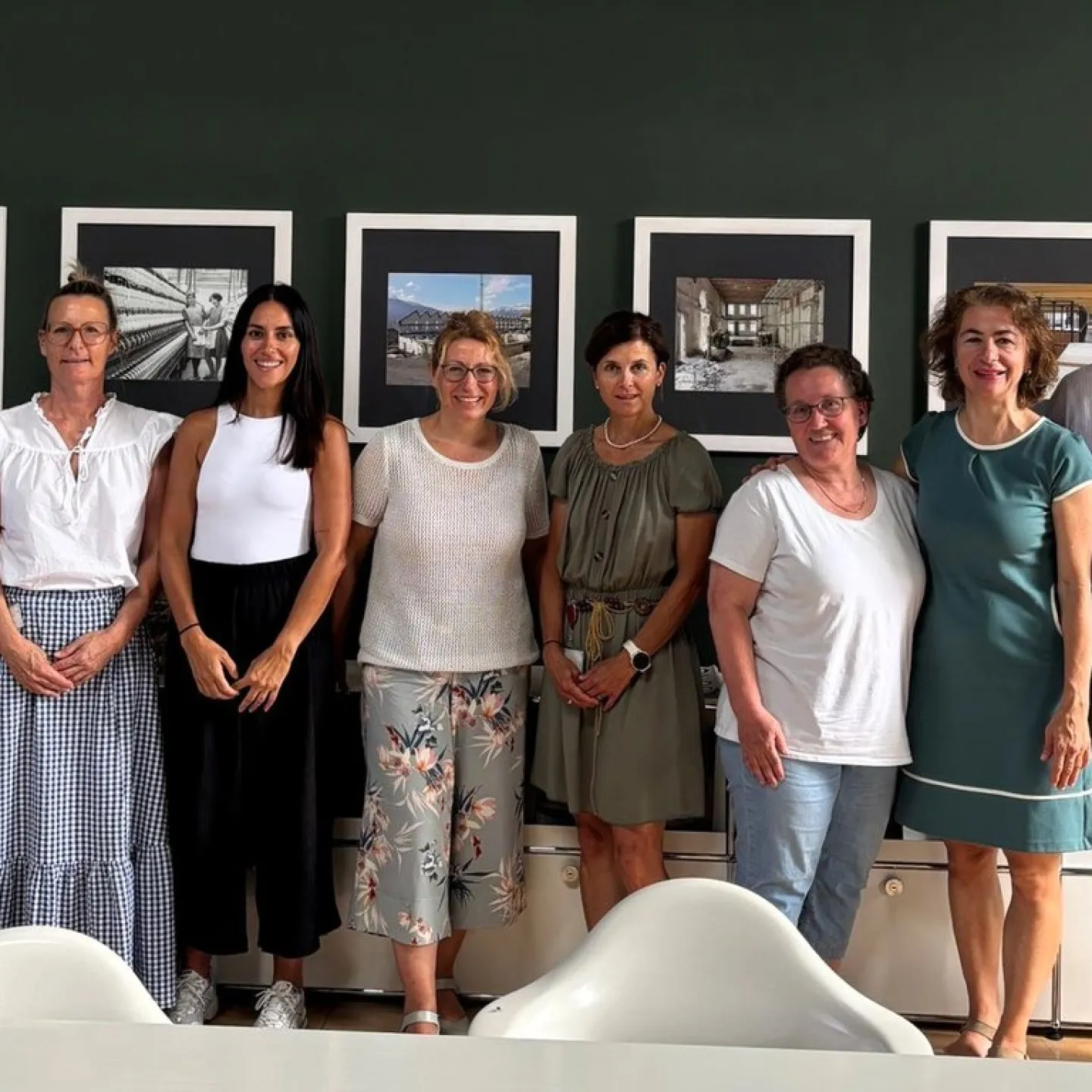 Eine Gruppe von acht Personen steht lächelnd vor einer Wand mit gerahmten Bildern. Sie befinden sich in einem Besprechungsraum der Universität Liechtenstein.