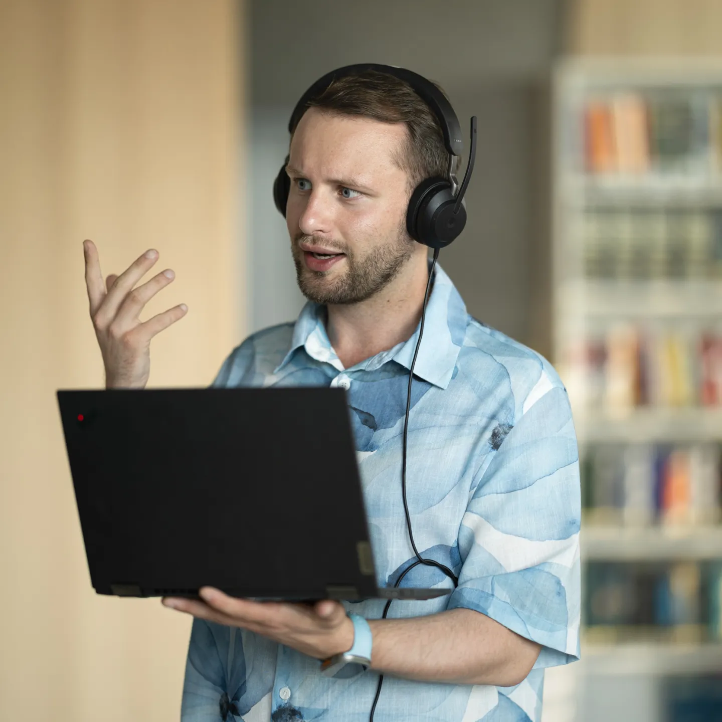 Student mit Laptop und Headset im Bibliotheksbereich der Universität Liechtenstein während eines Online-Meetings.
