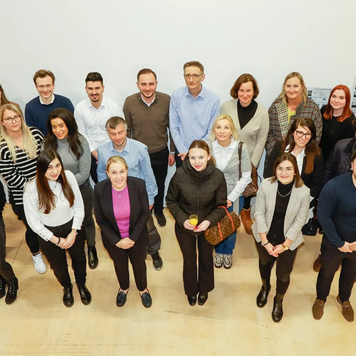 Teilnehmende des Zertifikatsstudiengangs Treuhandwesen an der Universität Liechtenstein stehen in einer Gruppe zusammen und blicken nach oben. Sie sind in einem hellen Raum mit neutralem Hintergrund.