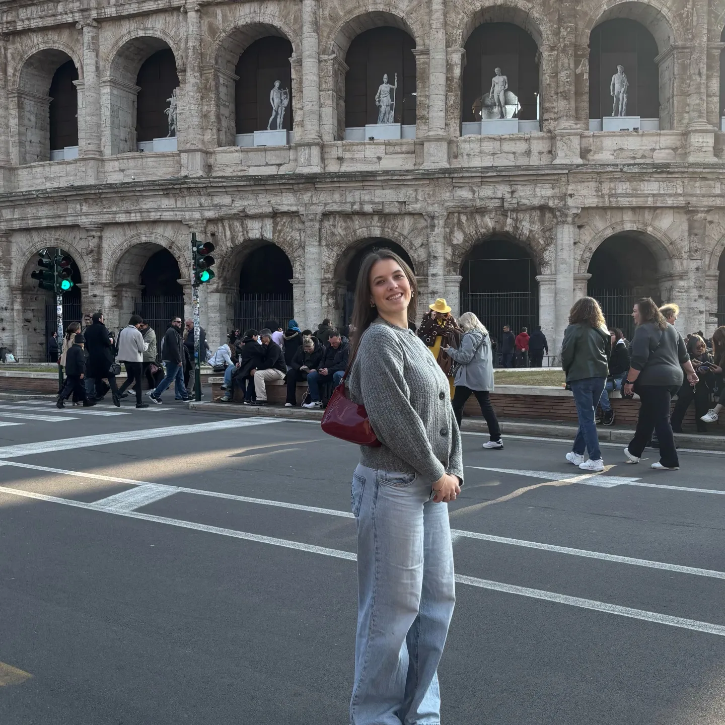 Frau steht lächelnd vor dem Kolosseum, während im Hintergrund Touristen an der Straße entlanggehen.