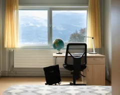 Wohnheimzimmer der Universität Liechtenstein mit Schreibtisch, Rucksack und Blick auf die Berge.