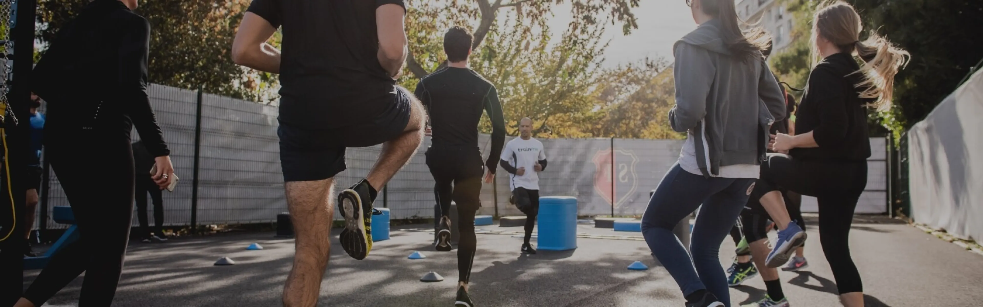 Eine Gruppe von  studierenden nimmt an einem Outdoor-Fitnesstraining teil. Sie laufen und trainieren gemeinsam auf einer gepflasterten Fläche mit Bäumen an der Uni Liechtenstein.