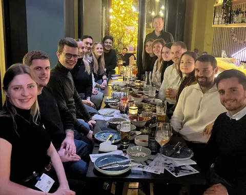 Eine Gruppe von Alumni der Universität Liechtenstein sitzt in einem Restaurant an einem langen Tisch, lächelnd und in geselliger Runde. Auf dem Tisch stehen Getränke und Teller mit Speisen. Die Atmosphäre ist warm und einladend.