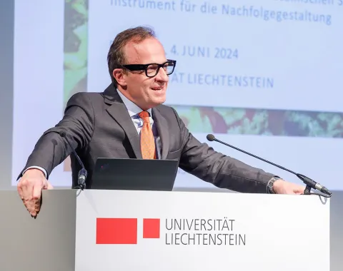 Ein Redner steht an einem Podium der Universität Liechtenstein und hält eine Präsentation. Im Hintergrund ist ein Bildschirm mit dem Datum 4. Juni 2024 zu sehen.