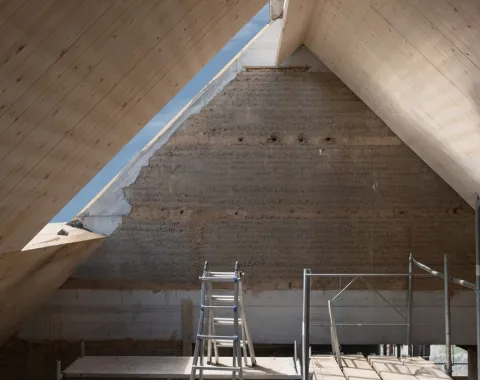 Innenansicht eines Dachbodens in Renovierung mit sichtbarer Holzkonstruktion und Gerüst. Natürliches Licht fällt durch ein Dachfenster.