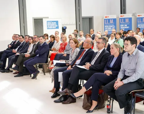 Eine Gruppe von Menschen sitzt in einem Konferenzraum der Universität Liechtenstein. Sie hören aufmerksam einem Vortrag zu. Im Hintergrund sind Banner mit der Aufschrift "LL.M." zu sehen.