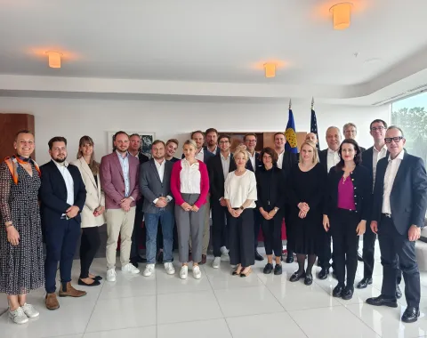 Gruppe von Studierenden und Dozenten des Executive Master of Laws (LL.M.) der Universität Liechtenstein während einer Studienreise in einem modernen Konferenzraum, im Hintergrund Flaggen.
