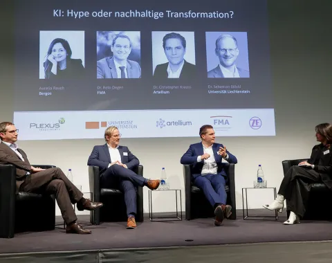 Eine Podiumsdiskussion an der Universität Liechtenstein über Künstliche Intelligenz mit vier Personen auf der Bühne. Im Hintergrund sind Porträts und Namen der Redner auf einer Leinwand zu sehen.